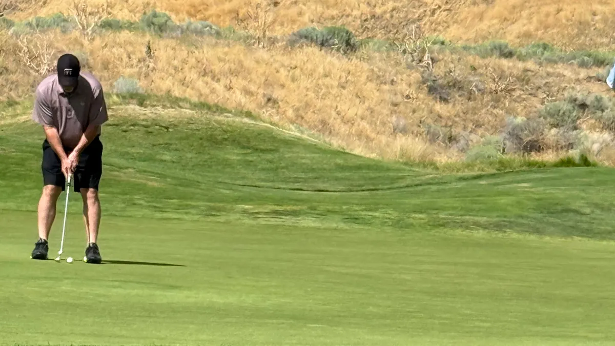 Sean lining up a putt on a green, with a sagebrush hillside rising behind it